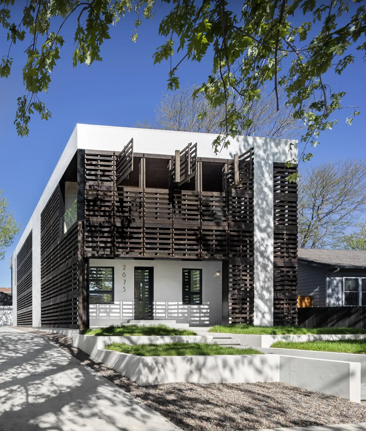 Front exterior view of Pallet House featuring white stucco walls and dark wood slat shading elements.