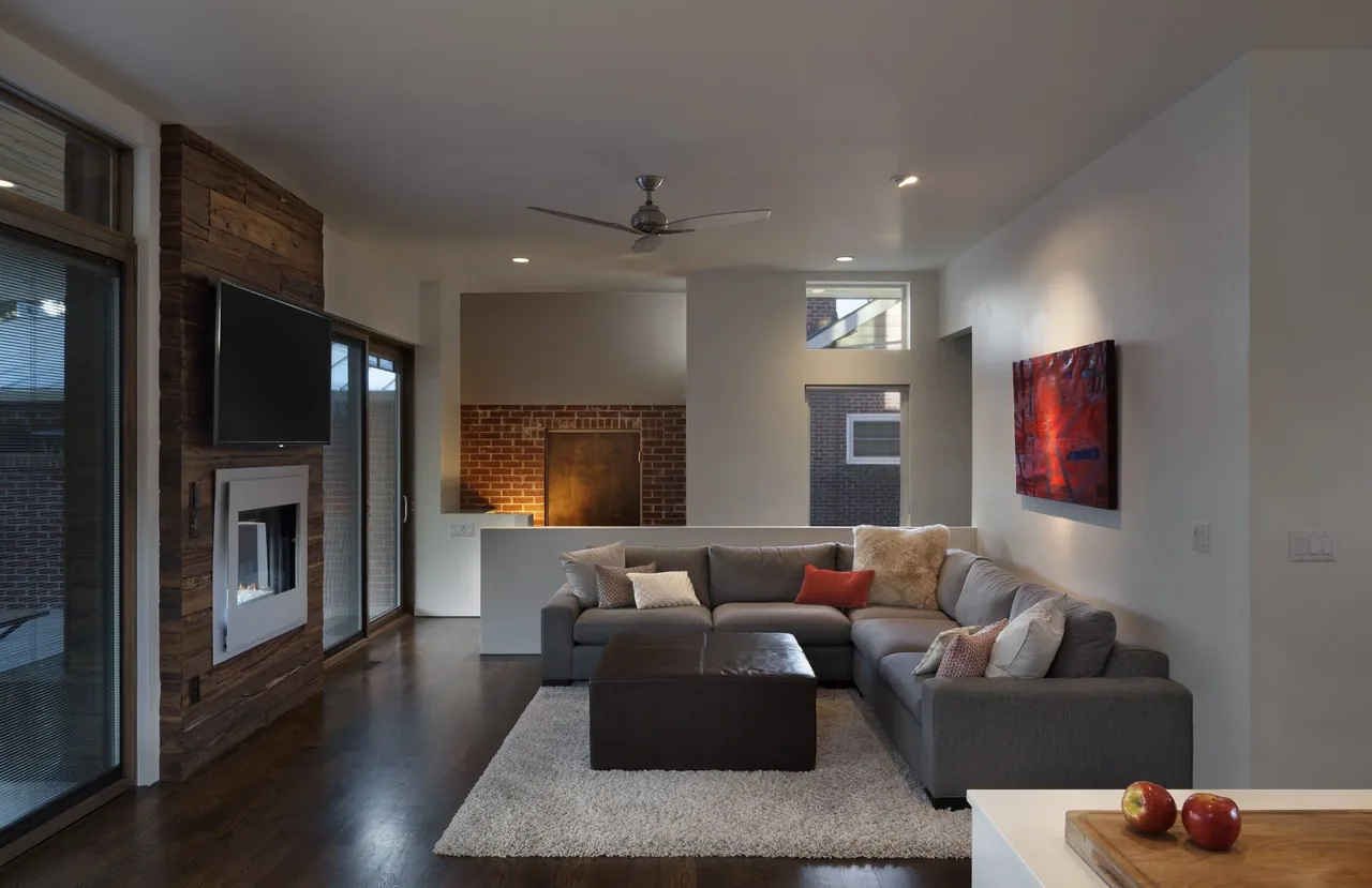 Interior view of a living room featuring a sectional sofa, fireplace with wood paneling, and wall-mounted TV.