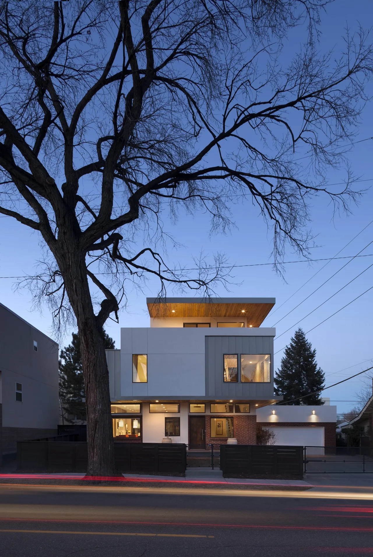 Modern three-story residence with cantilevered upper floor and a mix of brick, stucco, and metal siding.