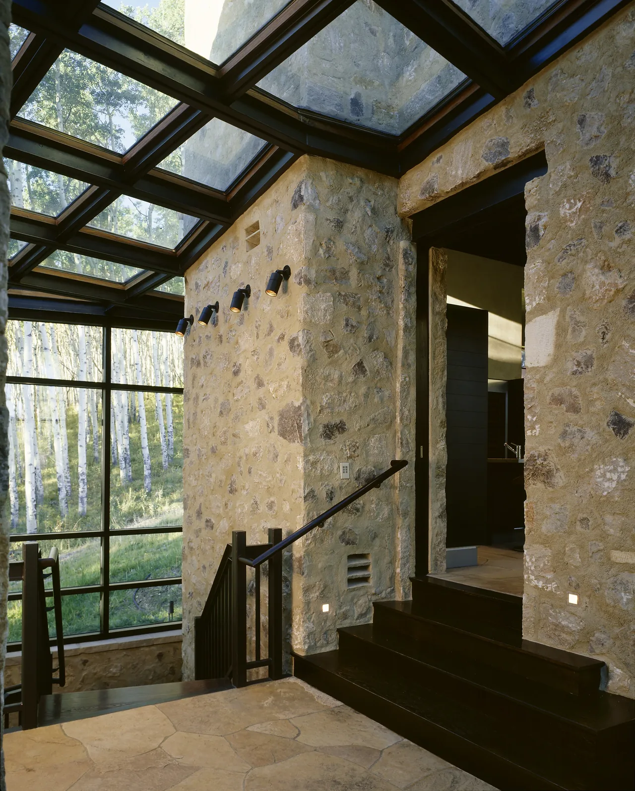 Stone walls and dark wood stairs contrast with large glass panels and exposed beams in the stairway area.