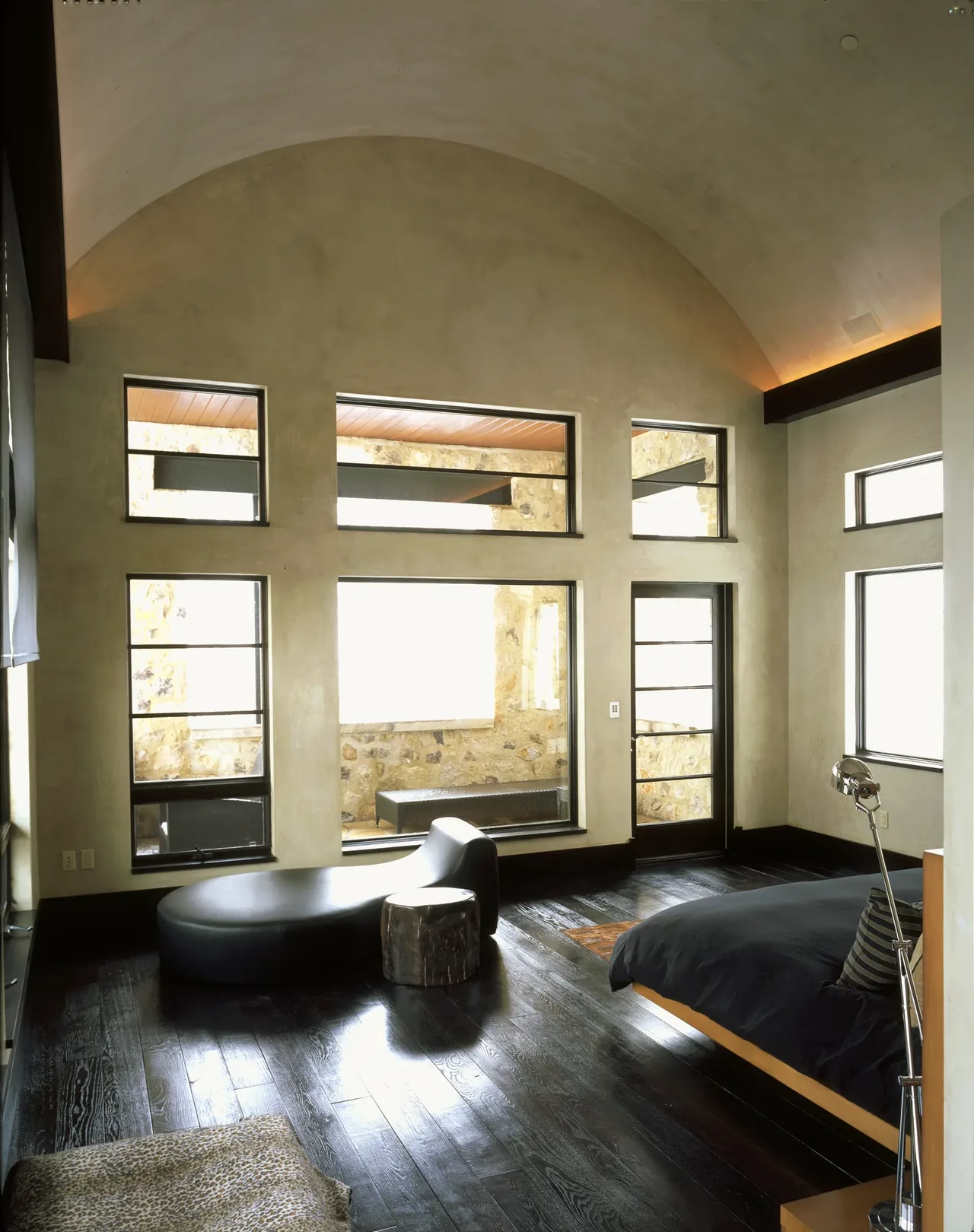 Bedroom features arched ceiling, multiple rectangular windows, and dark hardwood flooring.
