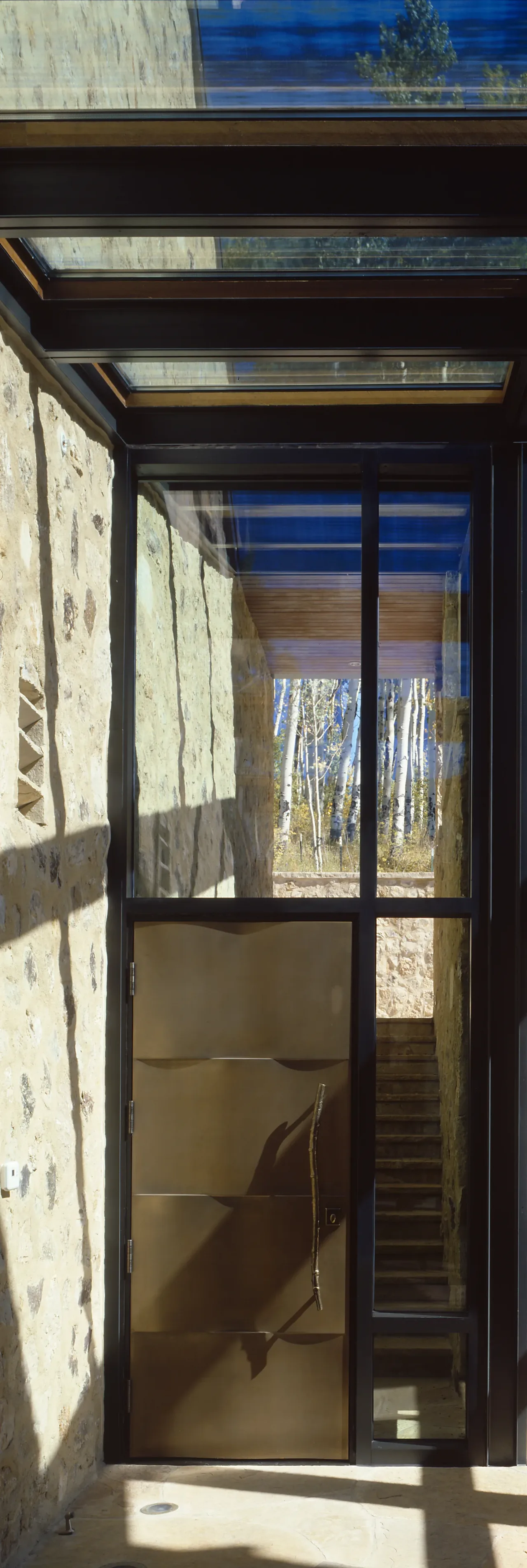 Entrance door features a metal panel door with a branch-shaped handle, surrounded by glass panels and stone walls.