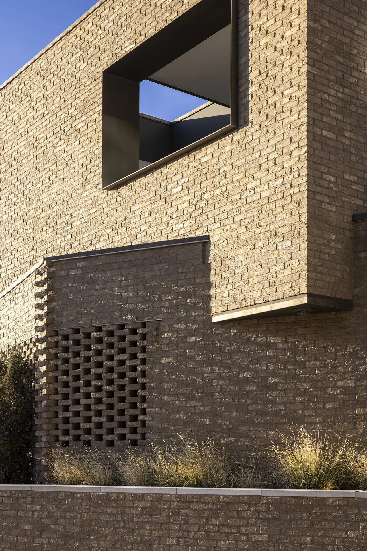 Exterior view of beige brick wall with a large recessed rectangular window and ventilated brick section.