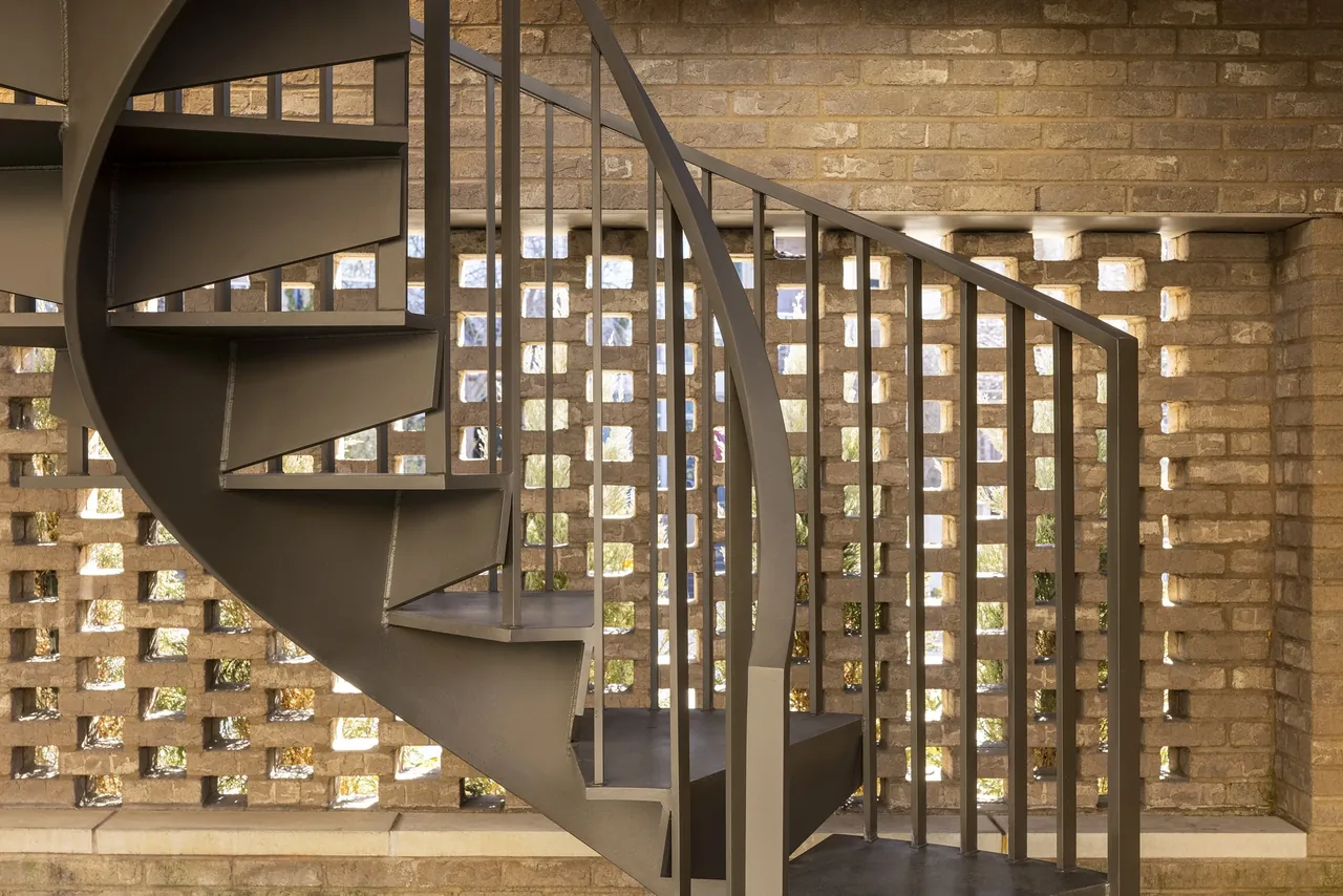Metal spiral staircase beside a perforated brick exterior wall allowing light penetration.