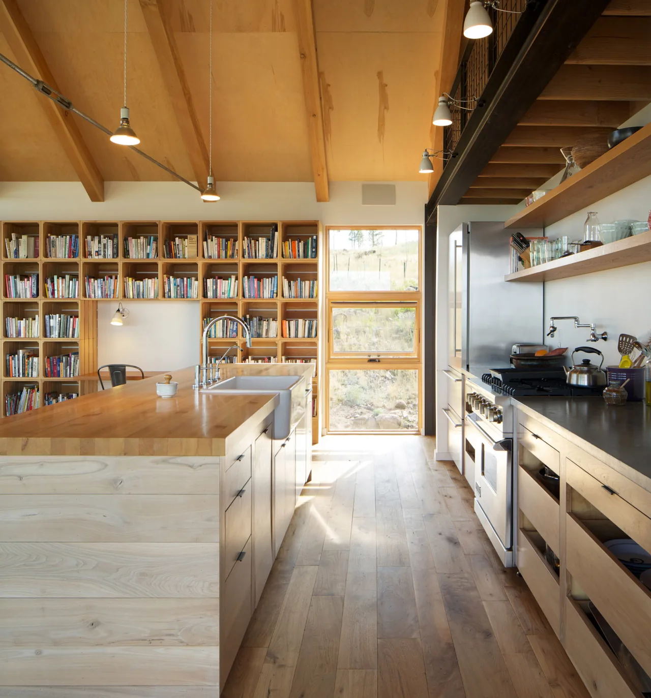 Kitchen space featuring a vaulted ceiling with exposed beams and floor-to-ceiling wooden shelving filled with books.