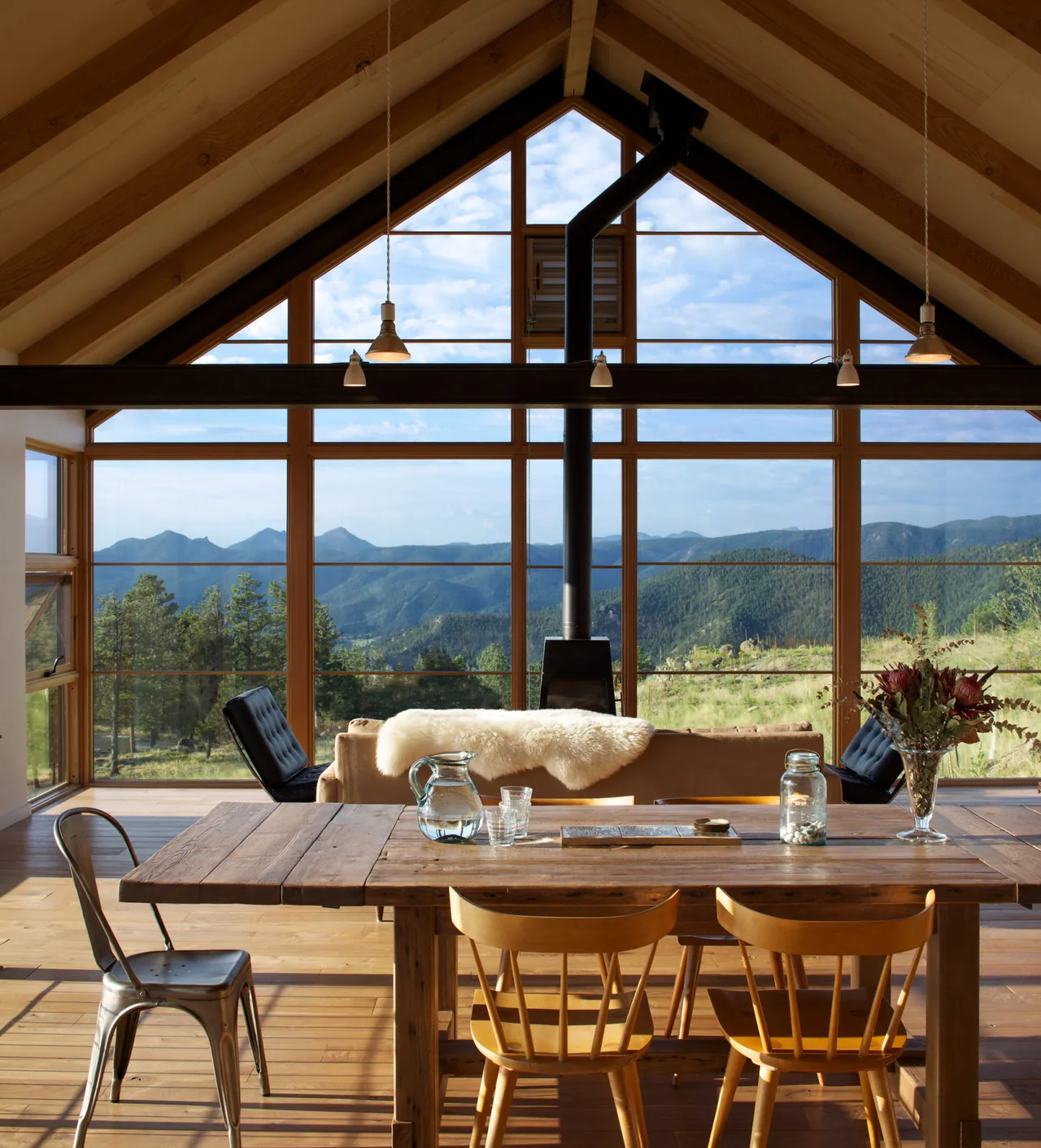 Living area with floor-to-ceiling glazing offering mountain views under a vaulted ceiling with exposed wood beams.
