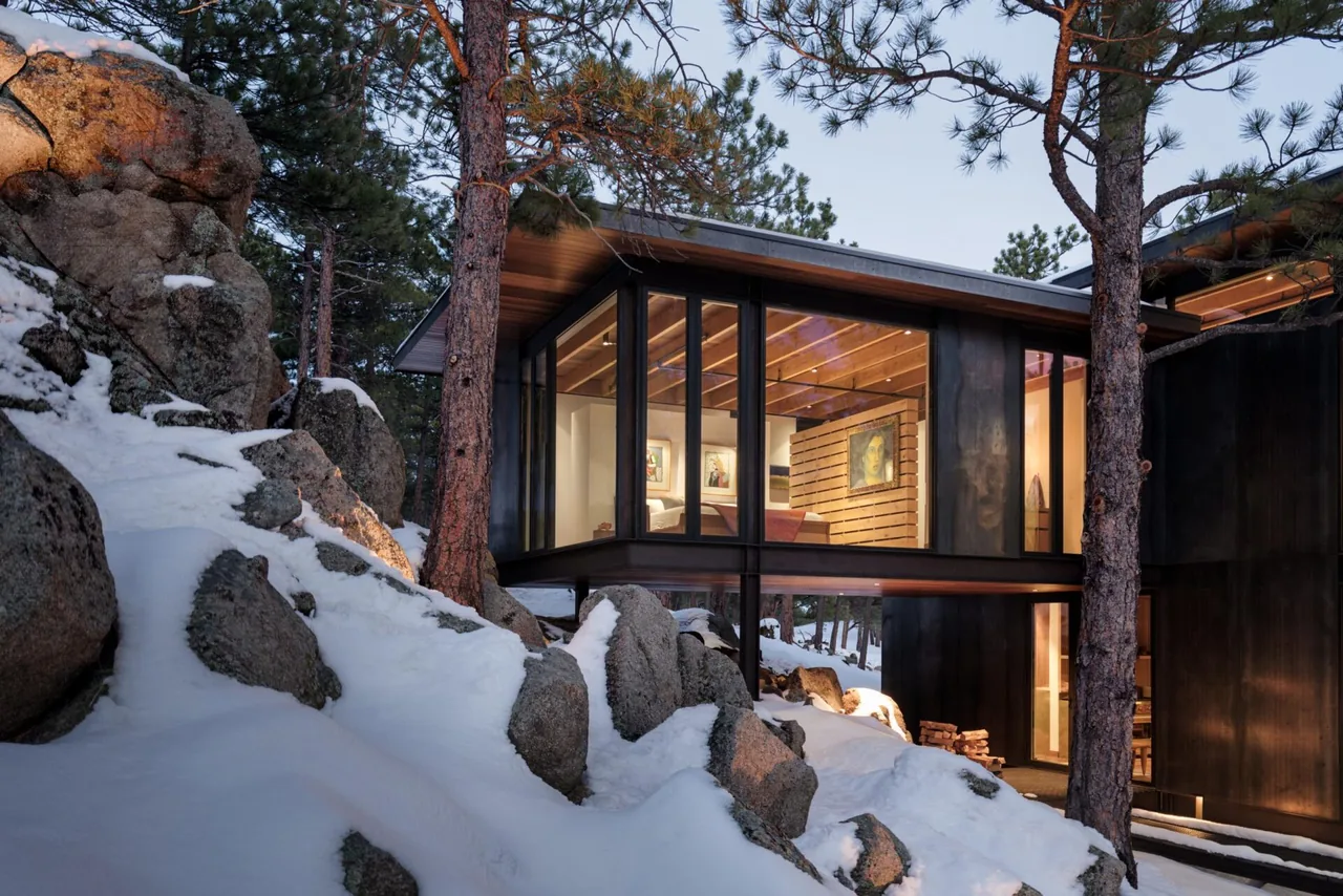 The Goatbarn Lane house features a cantilevered balcony with floor-to-ceiling glazing amid snowy pine trees.