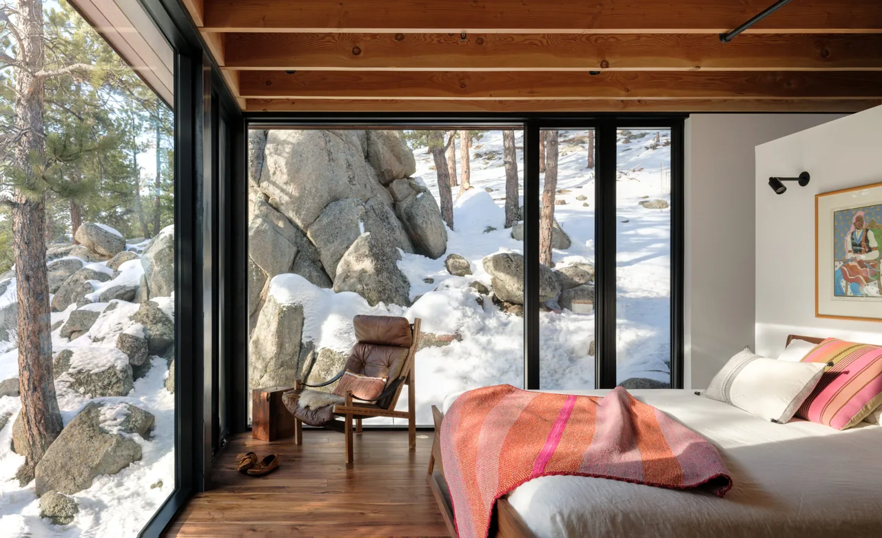 Bedroom with floor-to-ceiling black window frames reveals snowy rocky landscape outdoors.
