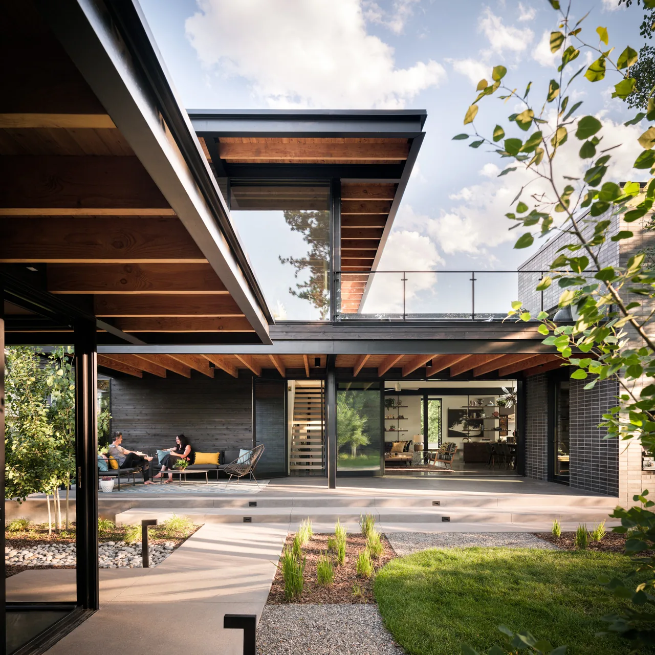 Exterior view of Mariposa Garden House showing wood ceiling beams, glass balcony railing, and landscaped yard with stone pathway.