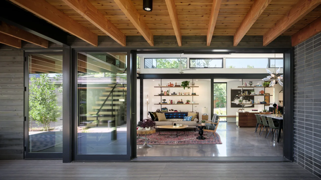 The Mariposa Garden House features an open living and dining area visible through sliding glass doors under exposed wood ceiling beams.