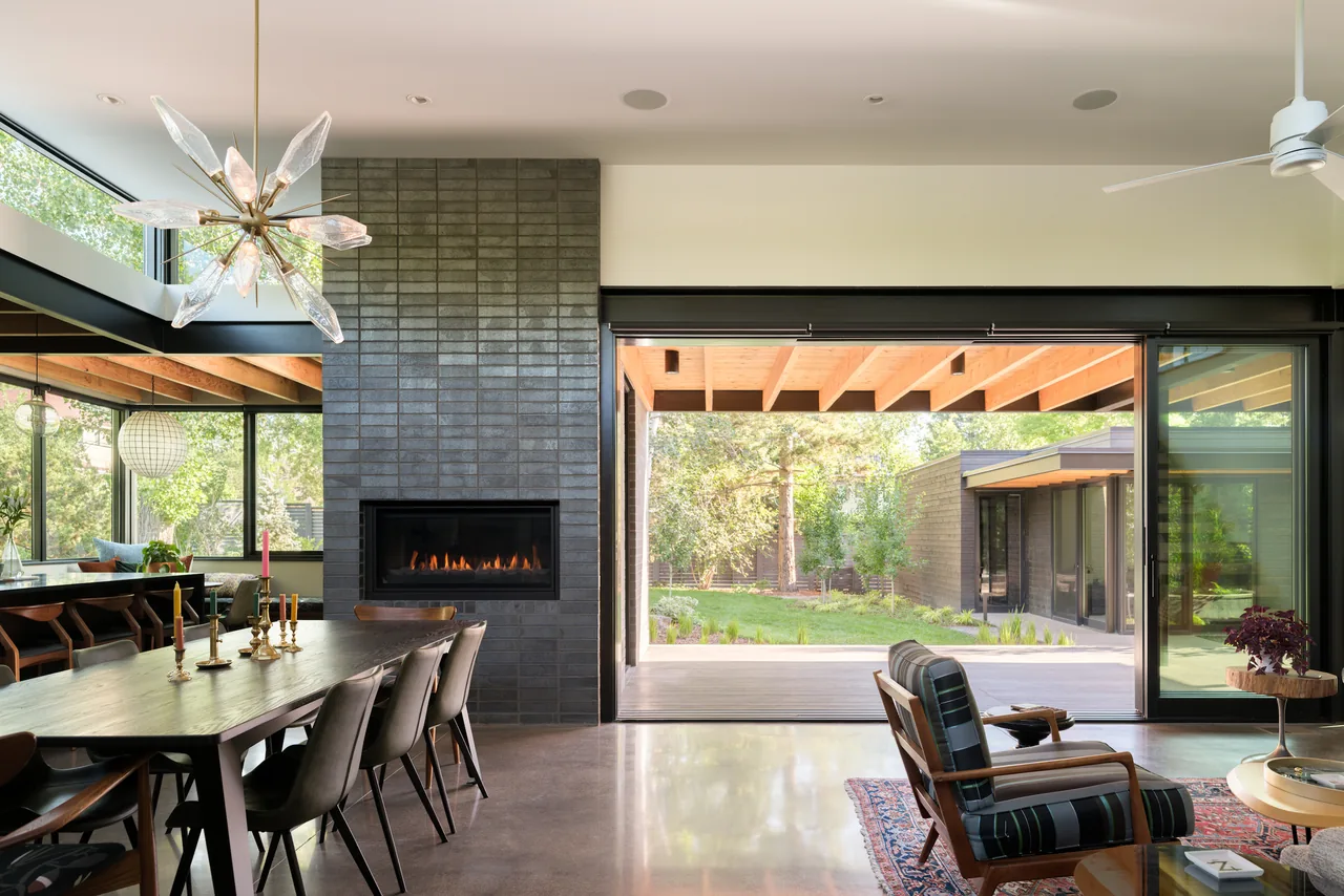 Dining and living spaces with dark tile fireplace and floor-to-ceiling glass doors opening to a garden porch.