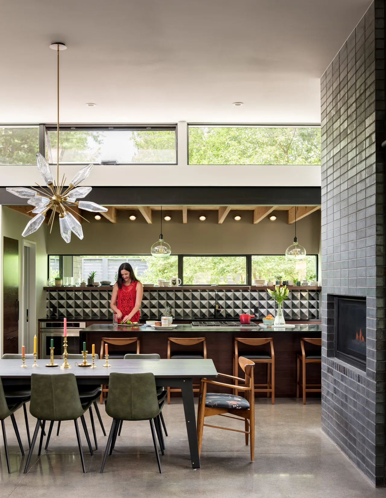 Open kitchen and dining space featuring geometric tiled backsplash, concrete floor, and a tiled fireplace wall with horizontal clerestory windows.