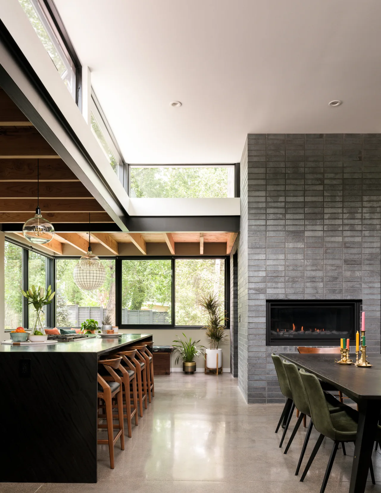 This open kitchen and dining area features a dark tile fireplace, exposed wood ceiling beams, and large windows for ample natural light.