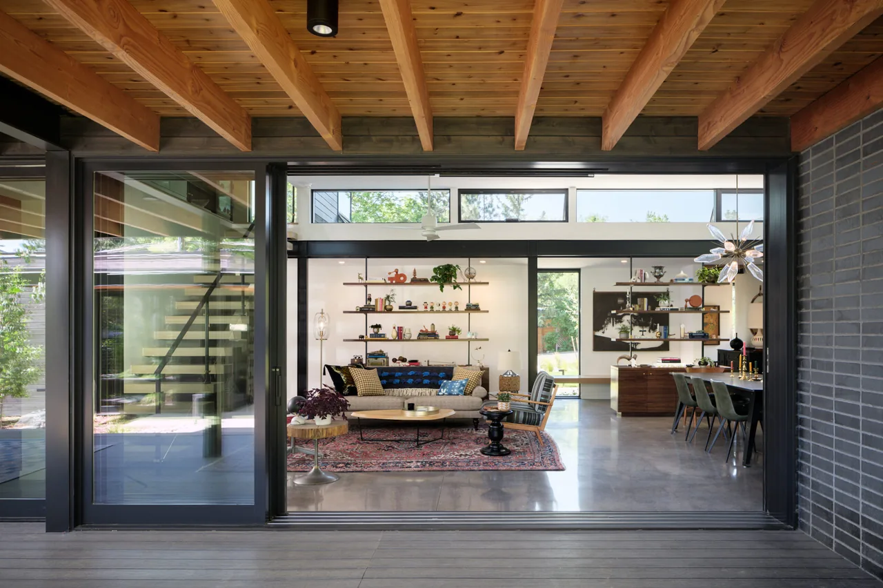 Living and dining space with large sliding glass doors, exposed beams, and a horizontal window band above.