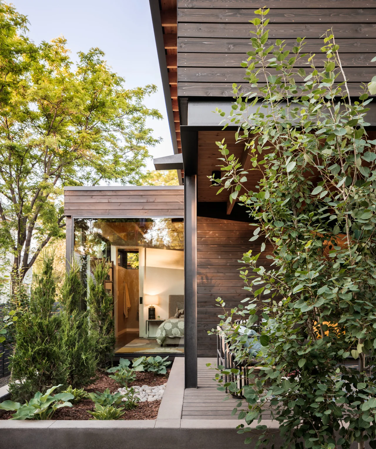 Corner of Mariposa Garden House showing dark wood siding, large windows, and a landscaped garden bed.