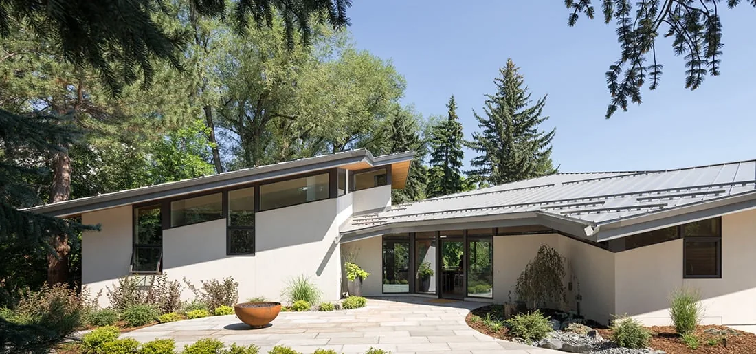 Gregory Creek Residence features a wood-paneled soffit and black steel window frames with a sloped standing seam metal roof.