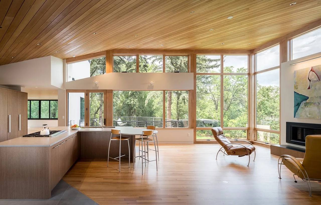 Open plan living and kitchen area with floor-to-ceiling windows and wood-paneled ceiling at Gregory Creek Residence.
