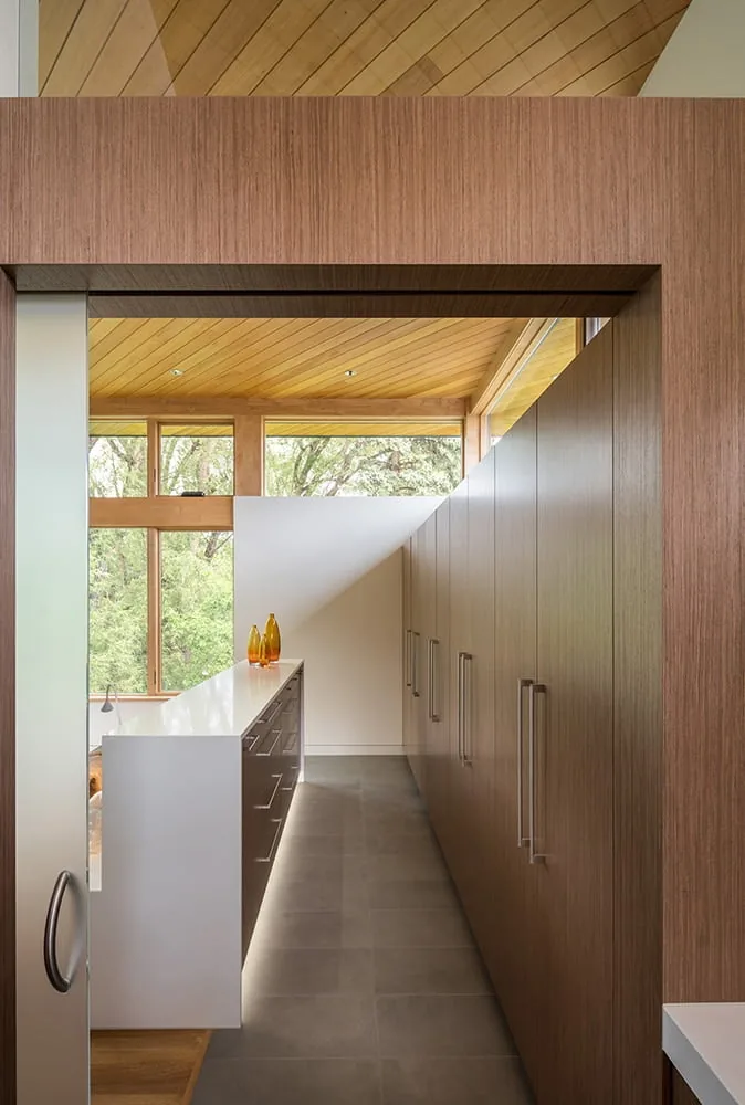 Pantry area with wood veneer cabinetry and white countertop island at Gregory Creek Residence by Gettliffe Architecture.
