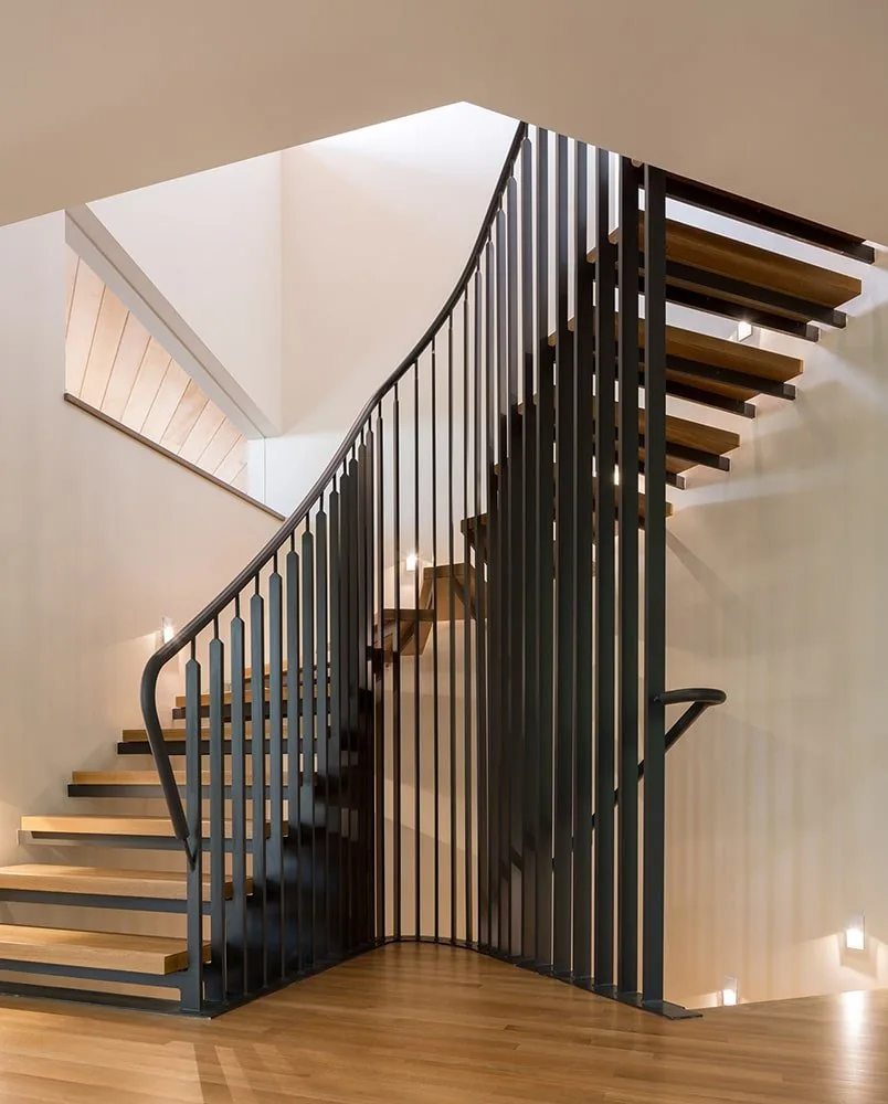 Floating wood stairs with curved black metal balustrade and angled ceiling at Gregory Creek Residence.