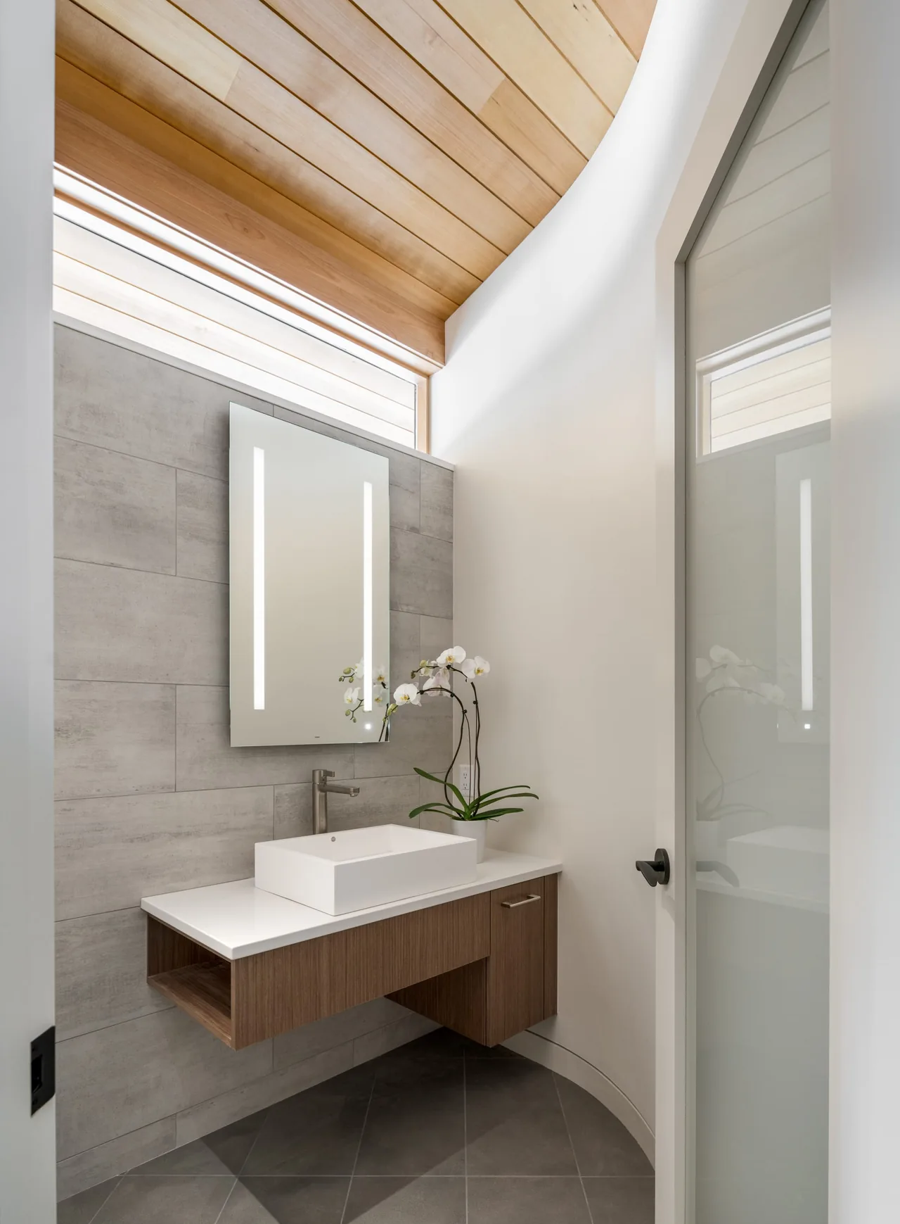 Bathroom interior featuring a floating wood vanity, wood-paneled ceiling, and large rectangular mirror with integrated light strips.