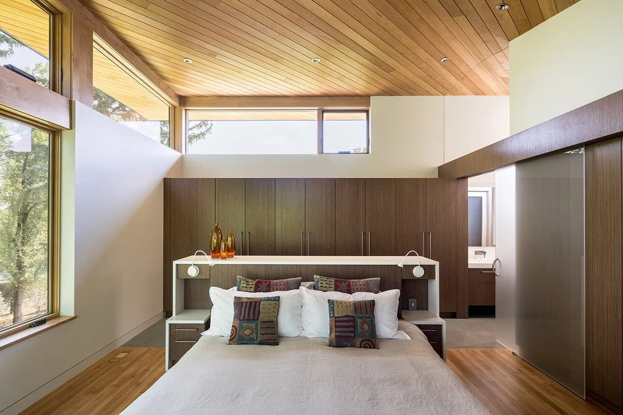 Bedroom featuring a wood-paneled ceiling, large windows, and built-in bedside shelving with pendant lights.