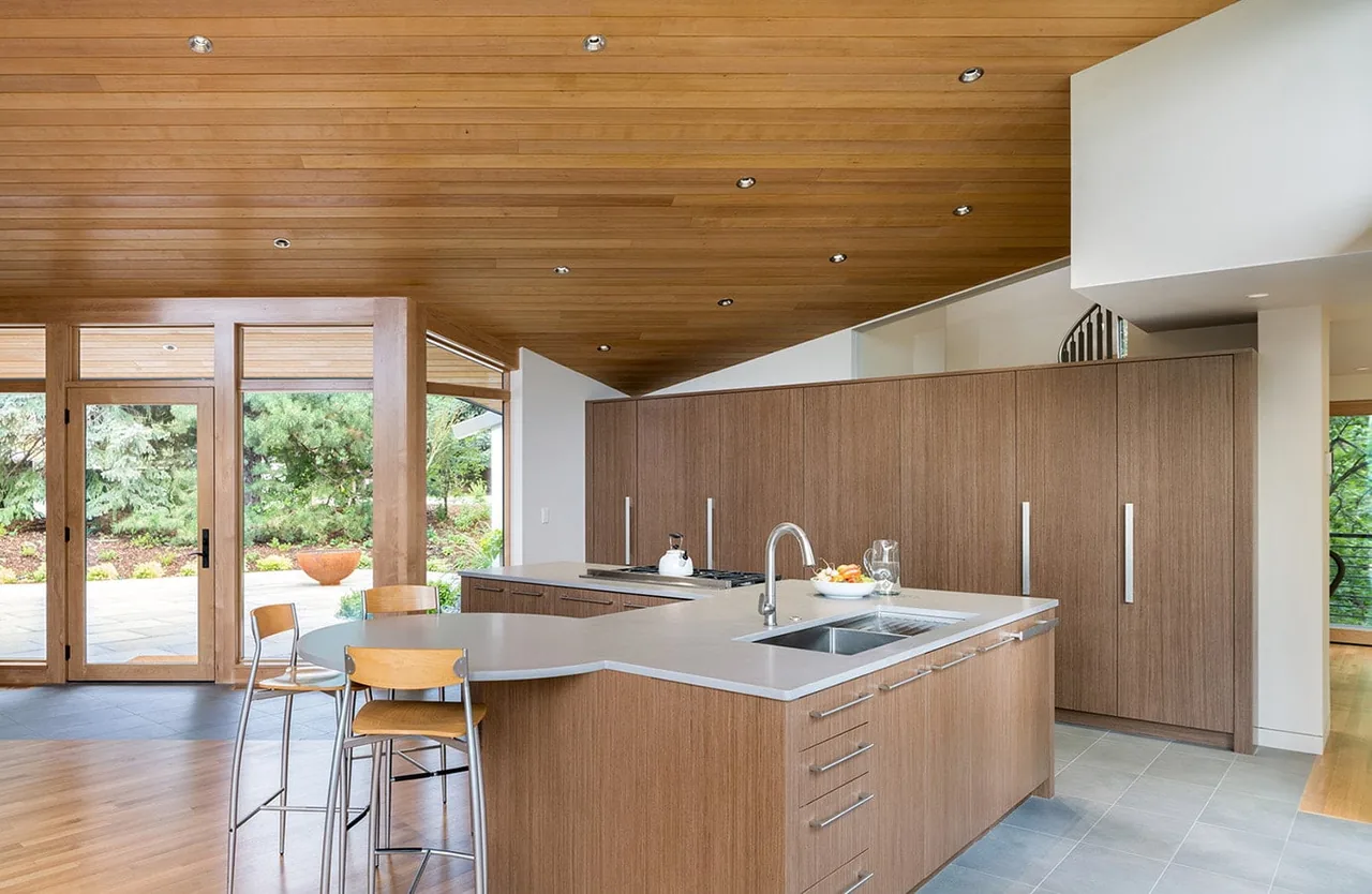 Gregory Creek Residence kitchen features a wood-paneled ceiling and an island with built-in sink and cooktop, designed by Gettliffe Architecture.