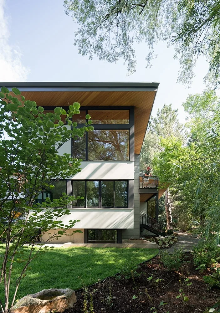 Exterior side view of the Gregory Creek Residence featuring large black-framed windows and a wood-paneled ceiling under the roof overhang.