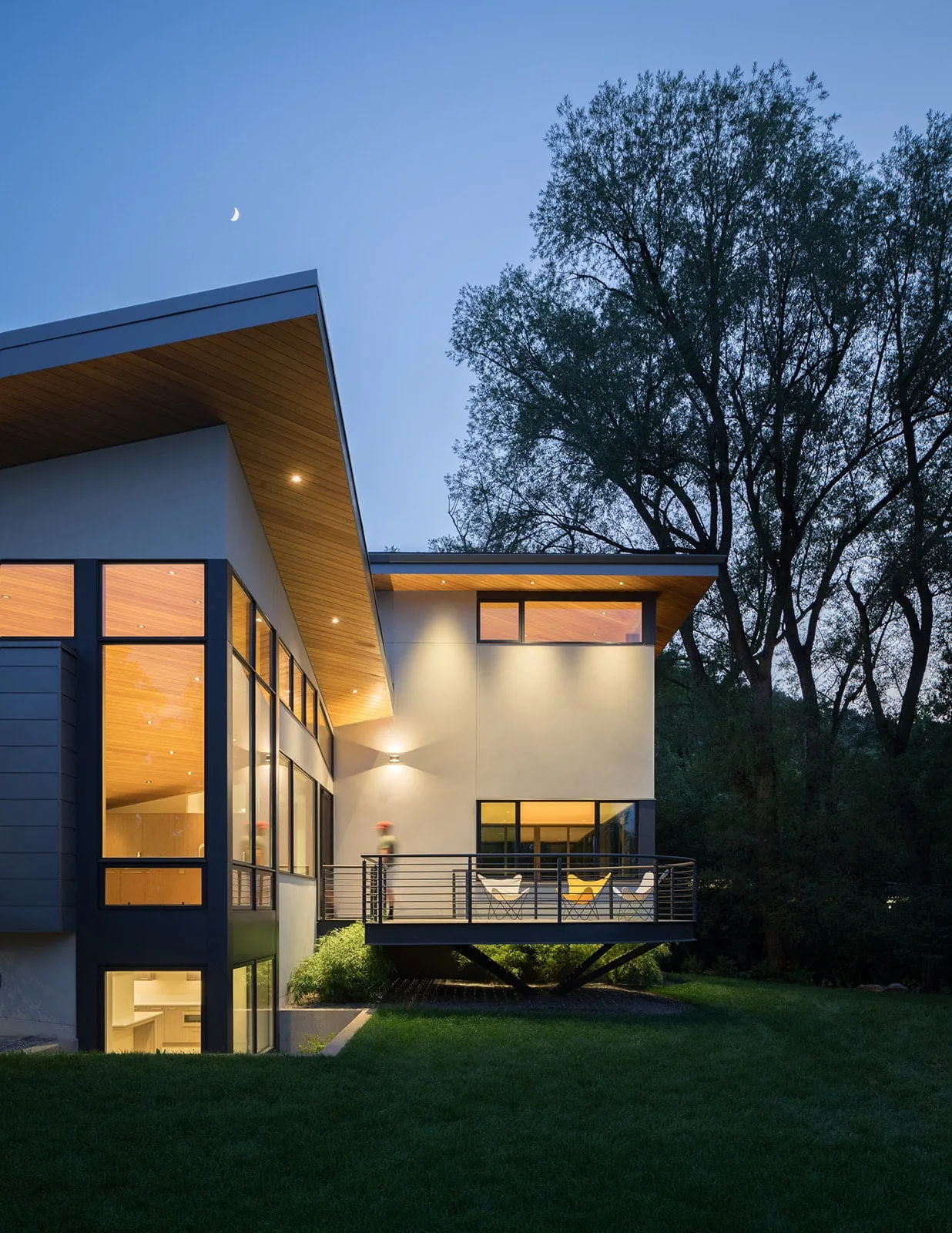 Gregory Creek Residence features a cantilevered balcony and expansive black window frames under a wood-paneled soffit.