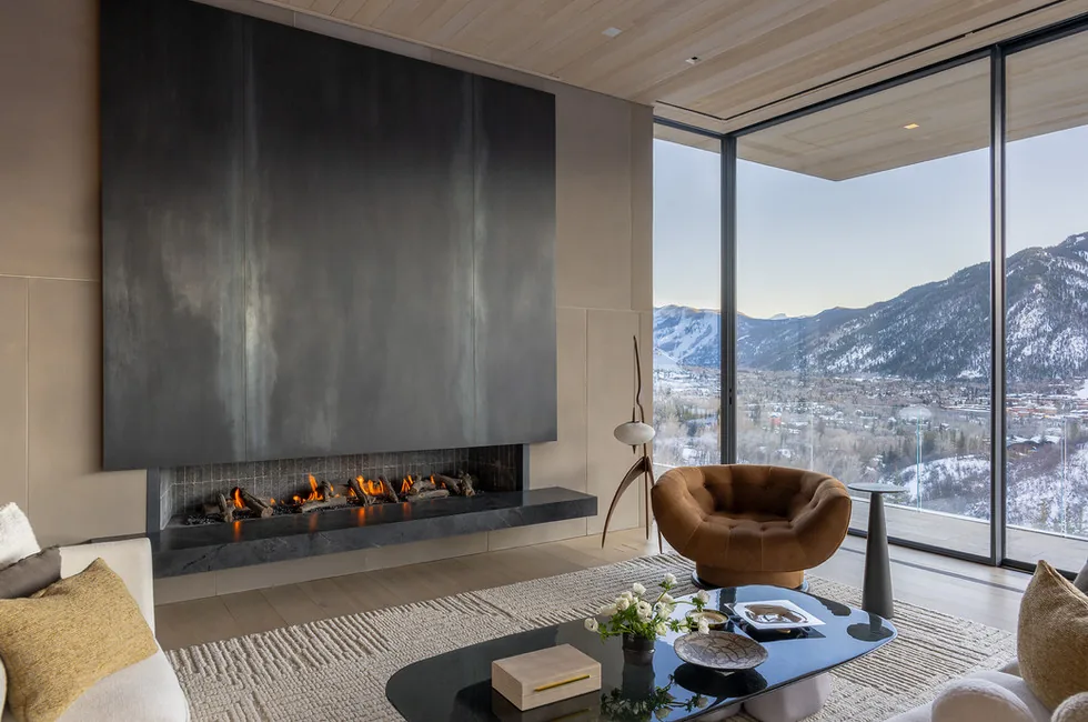 Living room featuring a large black gas fireplace and expansive floor-to-ceiling glazing overlooking snow-covered mountains.