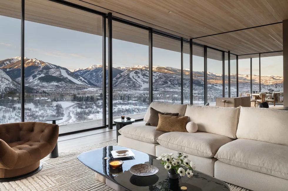 Living area with floor-to-ceiling glass walls offers views of snow-covered mountains in Sunshine Mountain project.
