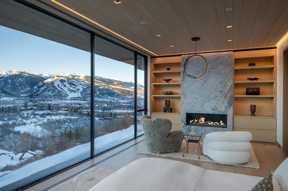 Living room featuring a modern fireplace, built-in shelves, and expansive glass walls overlooking snowy mountains.
