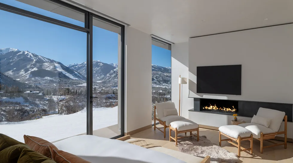 Sunshine Mountain living room with floor-to-ceiling windows revealing snowy mountain views and a linear fireplace below a wall-mounted TV.