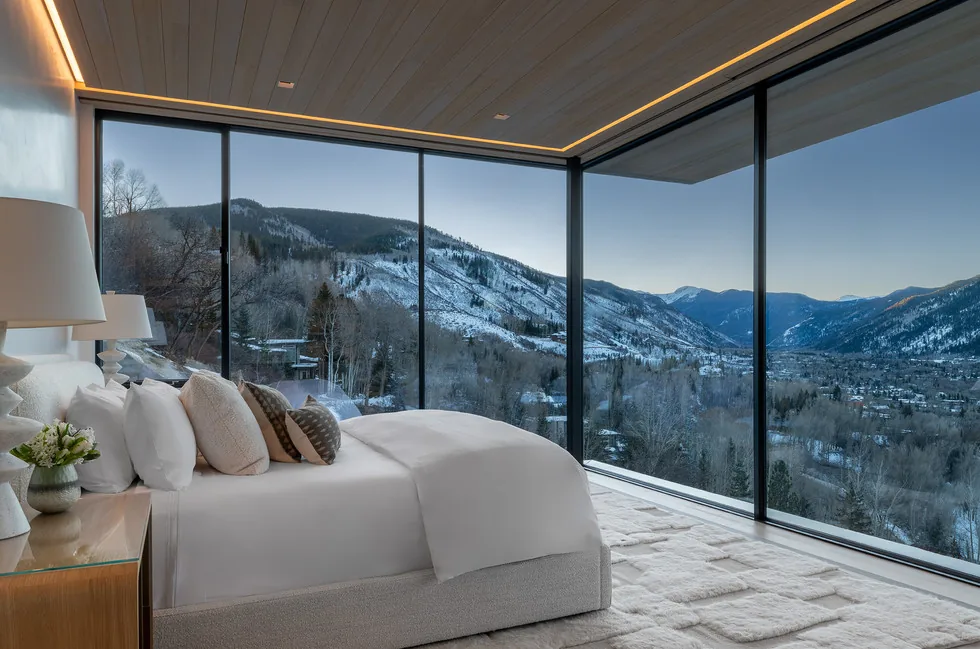 Bedroom with floor-to-ceiling glass walls showcasing a snowy mountain landscape.
