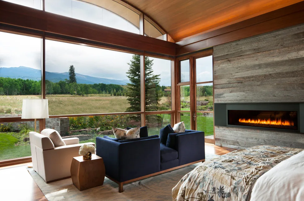 Living area featuring floor-to-ceiling windows with mountain views and a linear fireplace in a wood-paneled wall at Elk Peak Ranch.