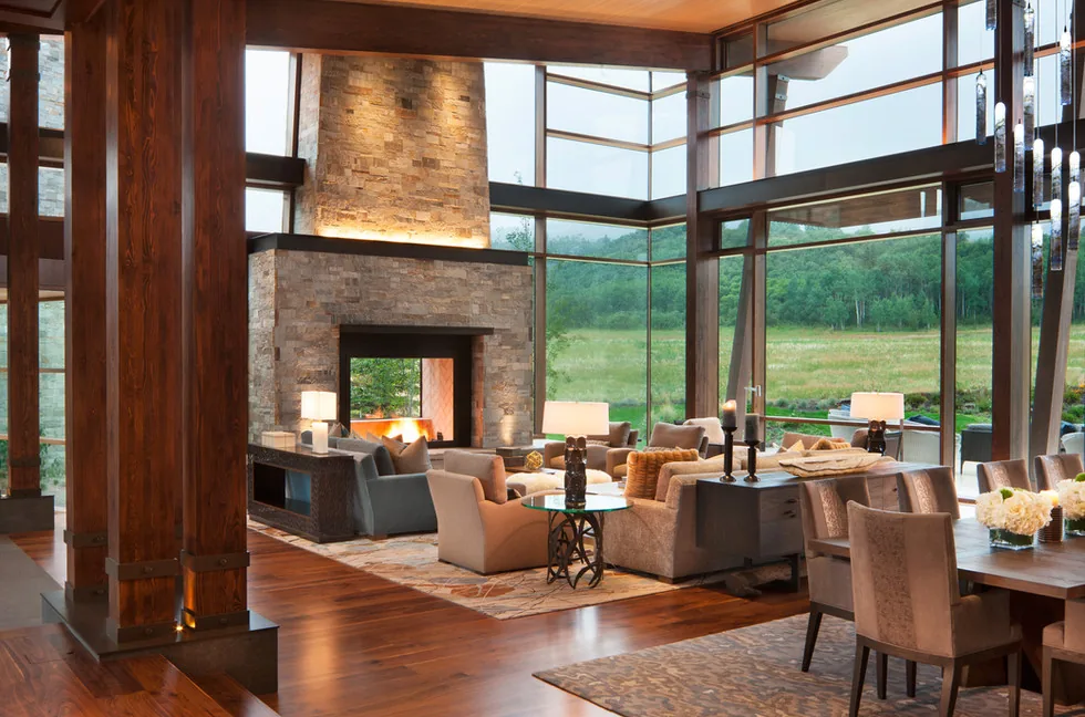 Living and dining space at Elk Peak Ranch with a stone fireplace, expansive glazing, and exposed wood beam columns.
