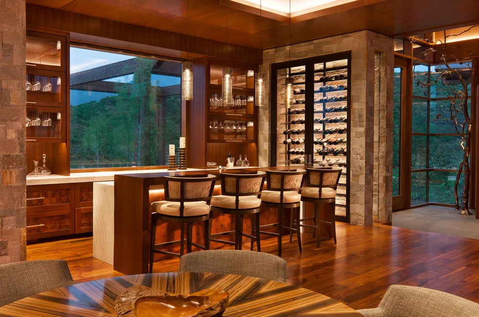 Residential bar area featuring wood paneled ceiling and walls, stone column, large windows, and built-in wine storage.