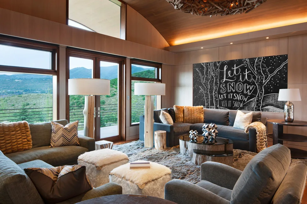 Living room at Elk Peak Ranch features wood-paneled walls and ceiling, large windows framing mountain views, and a cozy seating arrangement.
