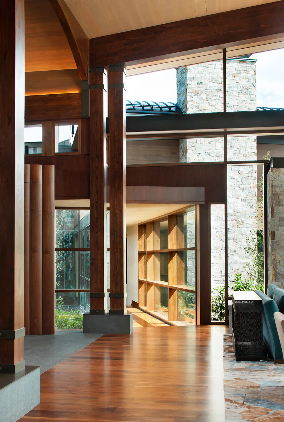 Interior view shows dark wood beams, a stone chimney, and large windows with sunlight illuminating wood and tile floors at Elk Peak Ranch.