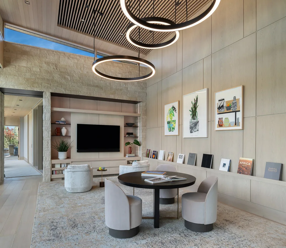 Living room with wood panel walls and ceiling, modern circular pendant lights, and built-in shelving with TV.