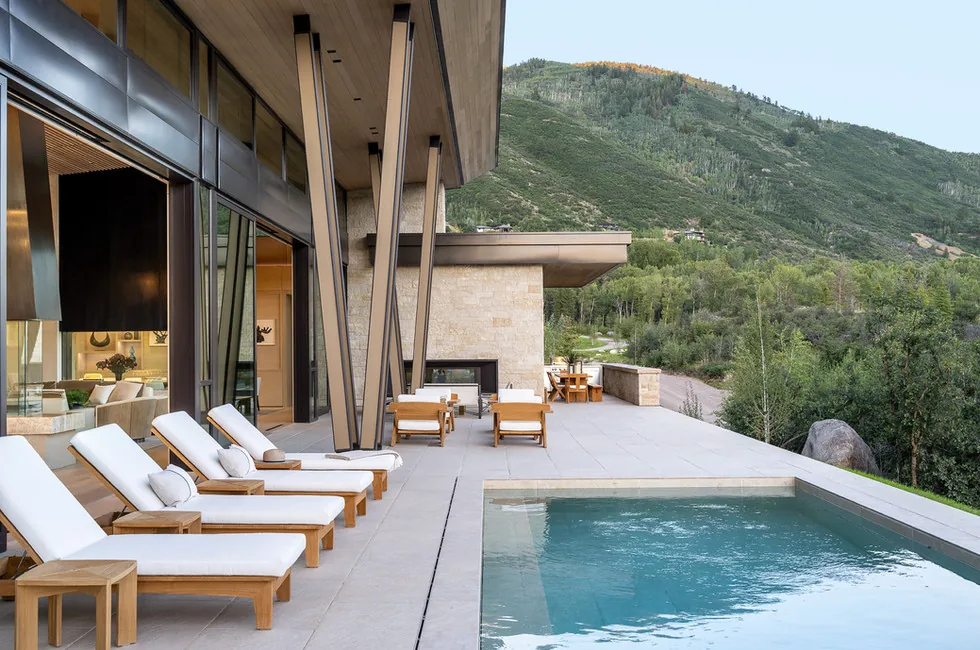 Outdoor patio with pool and lounge seating under an angled roof extension facing a hillside.