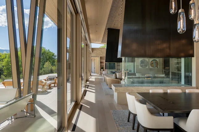 Modern living and dining area with floor-to-ceiling glass windows and vaulted ceiling showing outdoor patio.