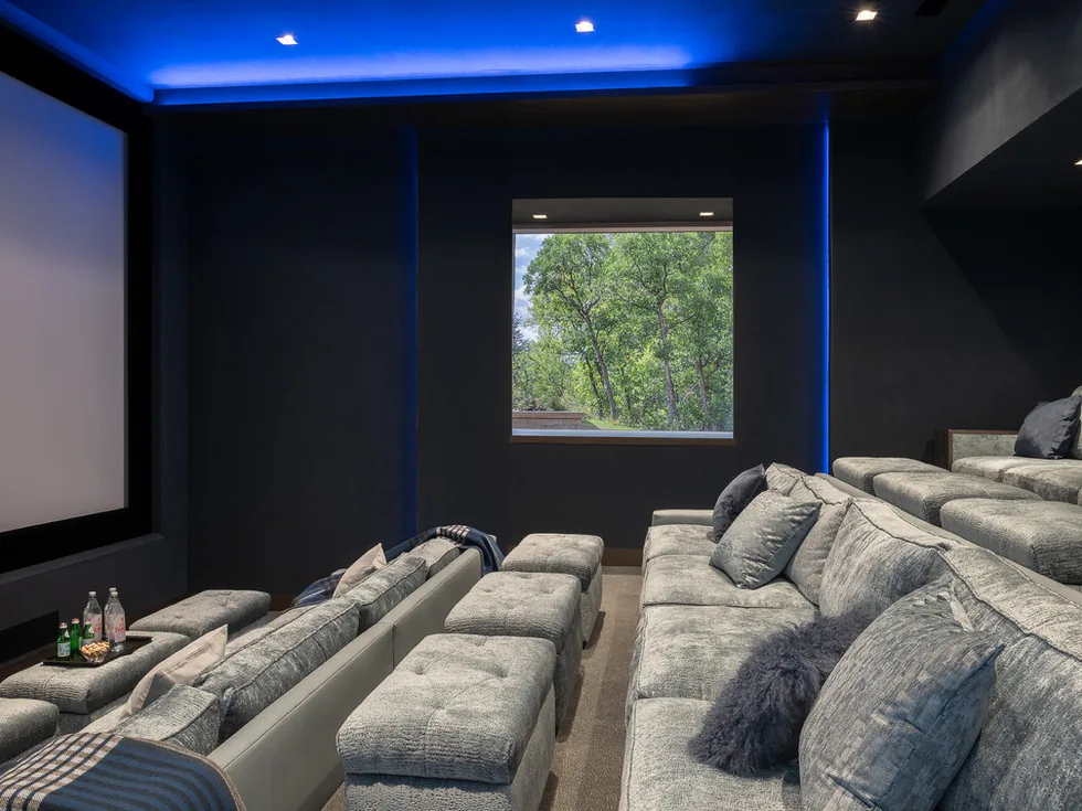 Tiered media room featuring gray upholstered sofas and a large projection screen beside a window.