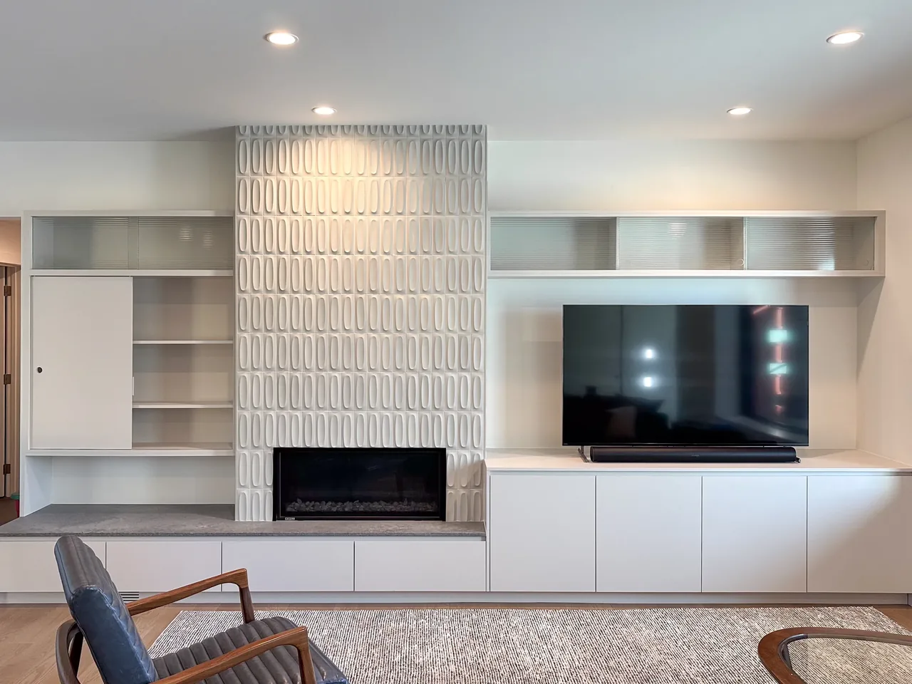Living room features a textured tile fireplace surround and built-in cabinetry with shelving, paired with a mounted flat-screen TV.