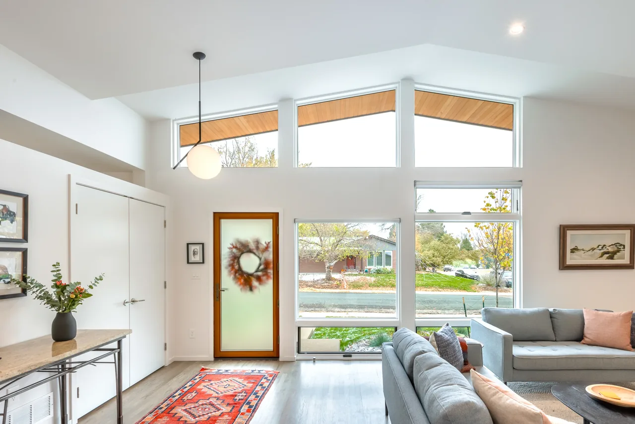 A modern living room featuring large triangular clerestory windows and a frosted glass front door with a wreath.