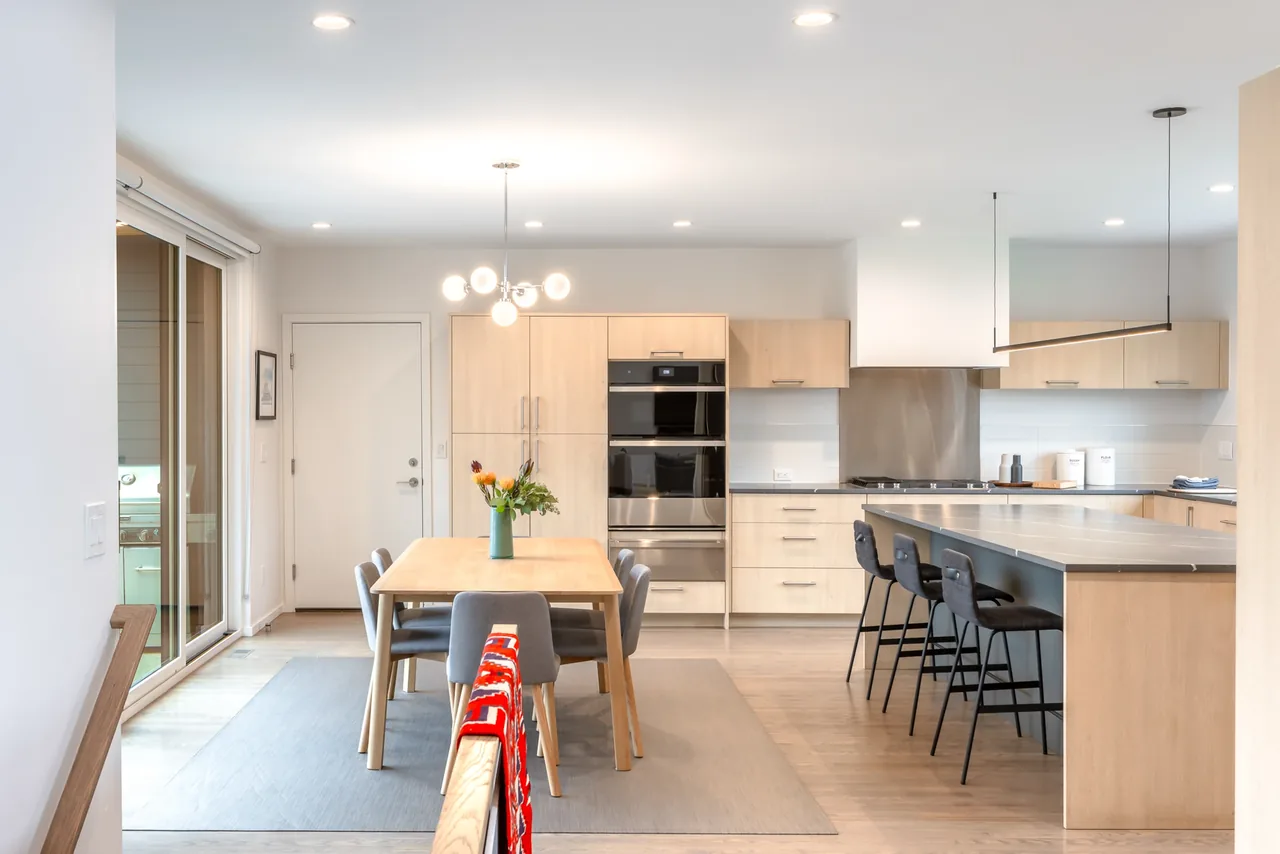 Modern kitchen and dining room featuring light wood cabinets, a gray kitchen island with bar stools, and recessed lighting.