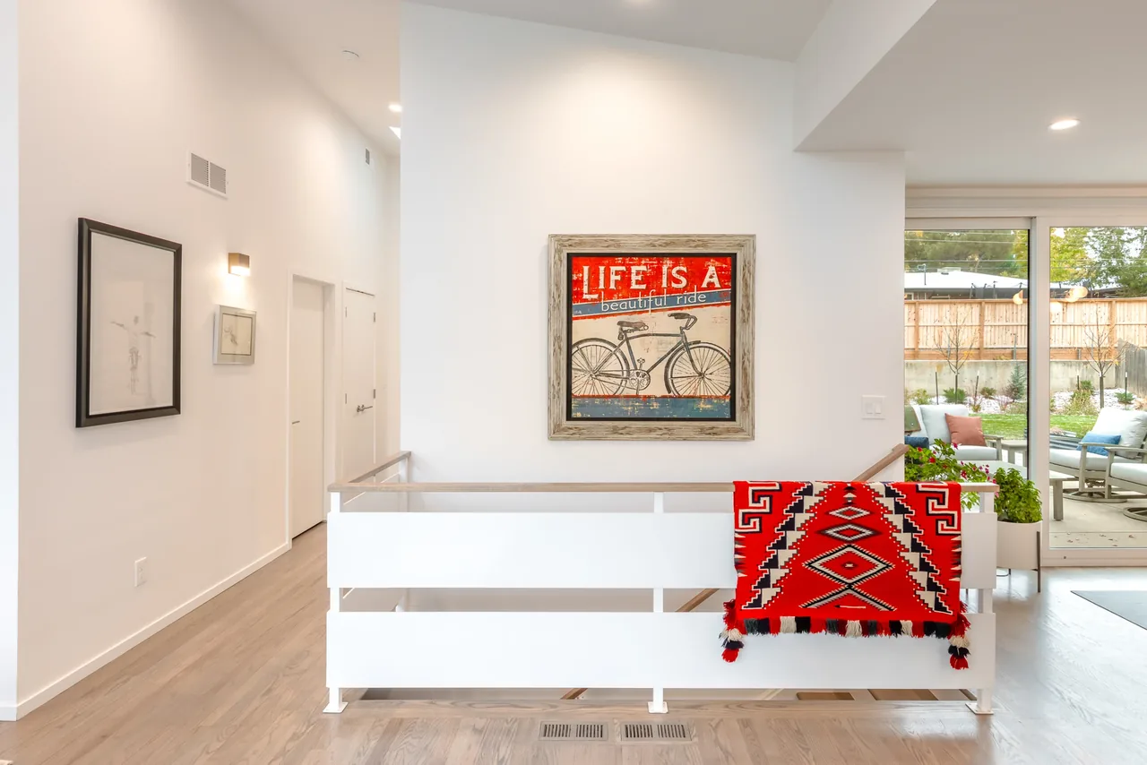 Hallway with light wood flooring, white walls, framed bicycle art, and sliding glass door to patio.