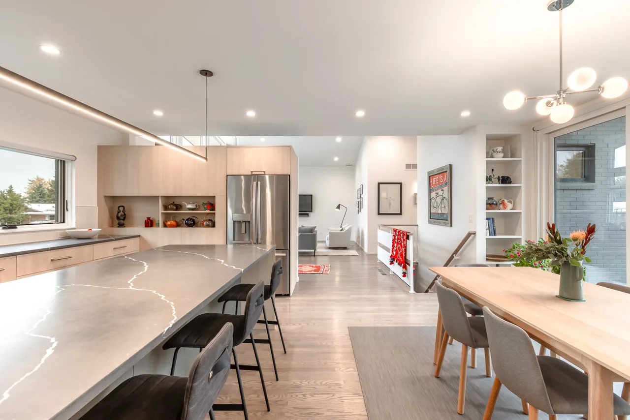Kitchen and dining room area in a modern home with a large island and wooden dining table under contemporary lighting.