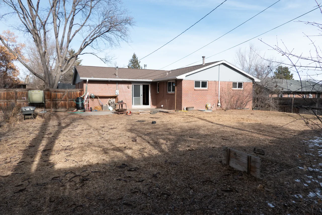 Rear exterior of a brick ranch-style home with a small concrete patio and bare trees surrounding the yard.