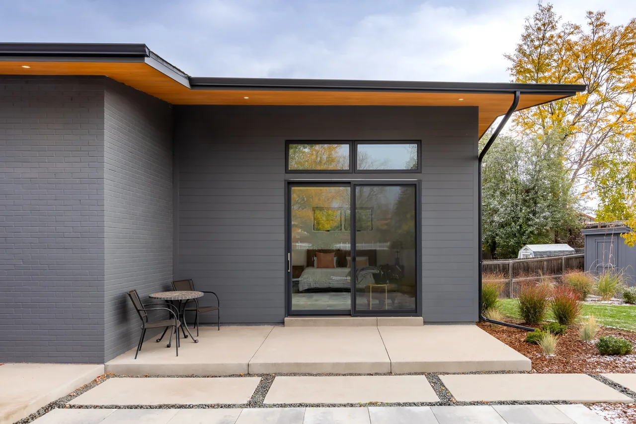 Modern single-story ranch exterior with dark gray siding, large sliding glass door, and concrete patio in backyard.