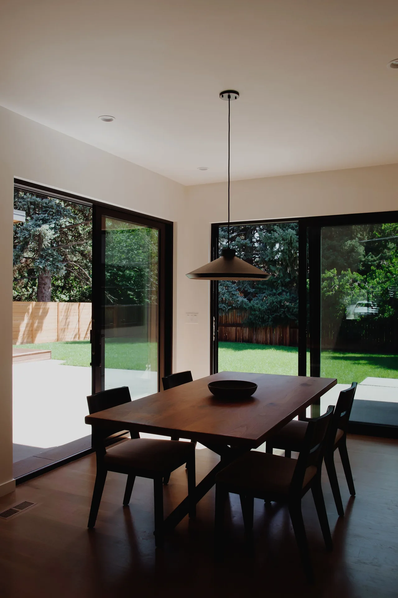 Dining room featuring a wooden table, dark chairs, pendant light, and large sliding glass doors to the outside yard.